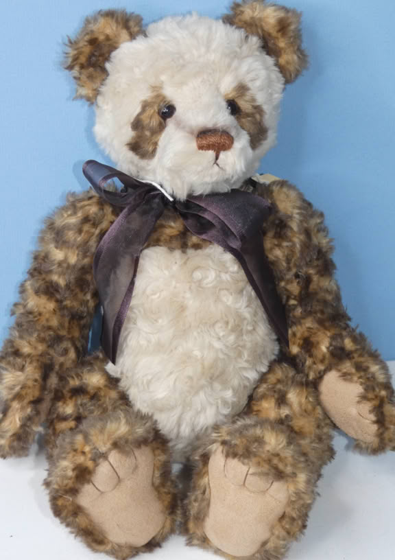 A plush teddy bear with a mix of white and brown fur, wearing a dark ribbon around its neck, sitting against a light blue background.