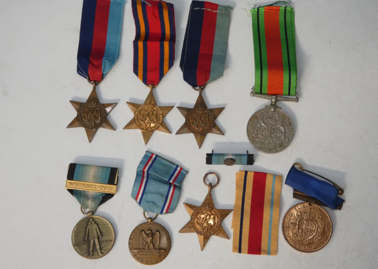 A collection of nine military medals with various ribbons, including star-shaped and circular designs, arranged on a white surface.