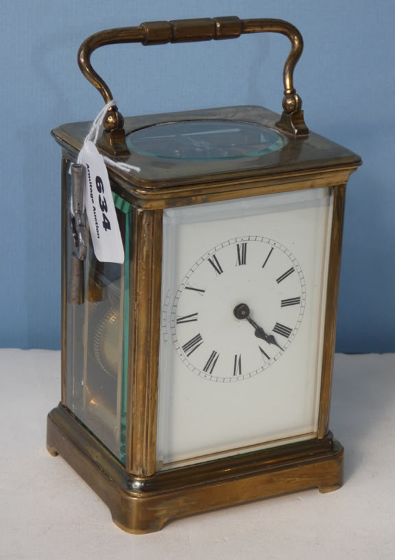A brass carriage clock with a white clock face, black Roman numerals, and a handle on top, placed against a blue background.