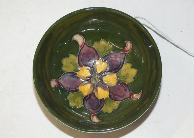 A round ceramic bowl with a green interior featuring a decorative floral pattern in the center, with purple and yellow petals.
