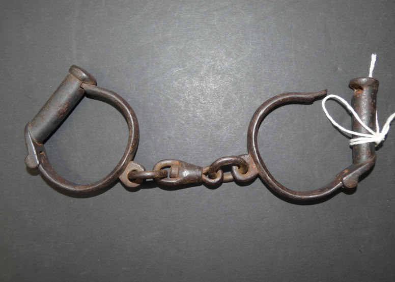 Old metal shackles with a chain and a white tag attached, set against a dark background.
