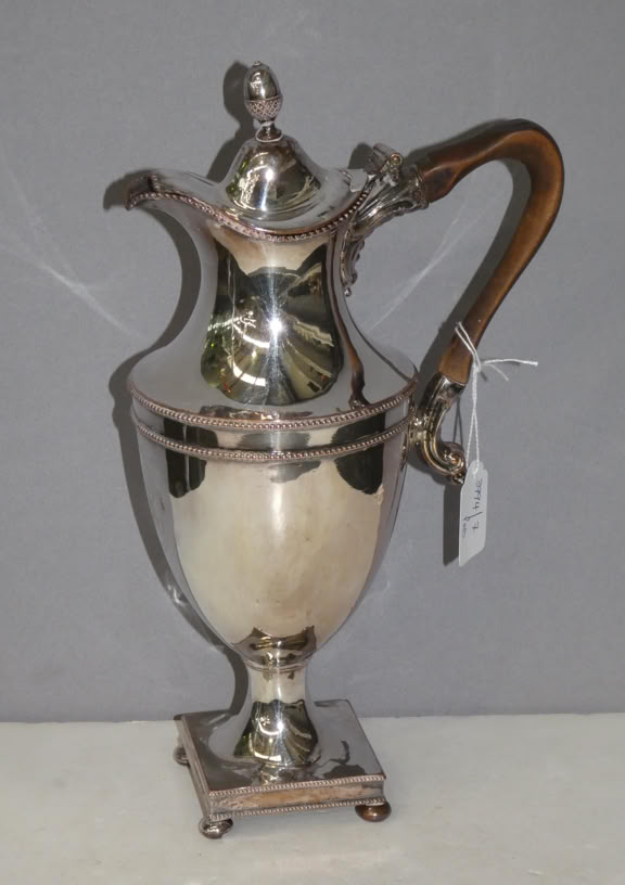 A silver teapot with a wooden handle and a decorative lid, placed on a flat surface against a plain background.