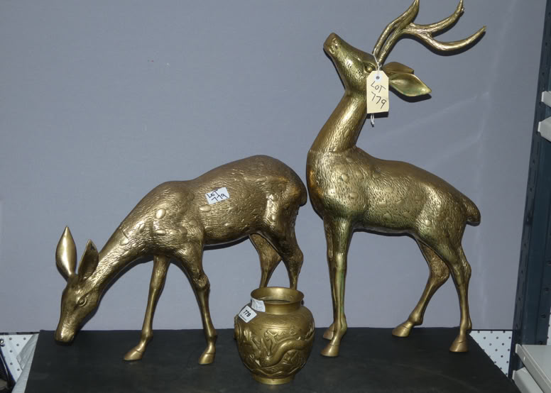 Two gold-colored deer sculptures, one with its head down and the other looking upward, with a small decorative pot in front of them.
