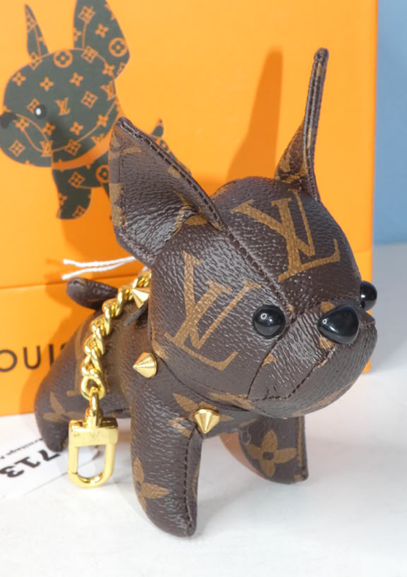 A small dog figurine with a brown and gold pattern resembling a luxury brand logo, standing in front of an orange box with a similar pattern.